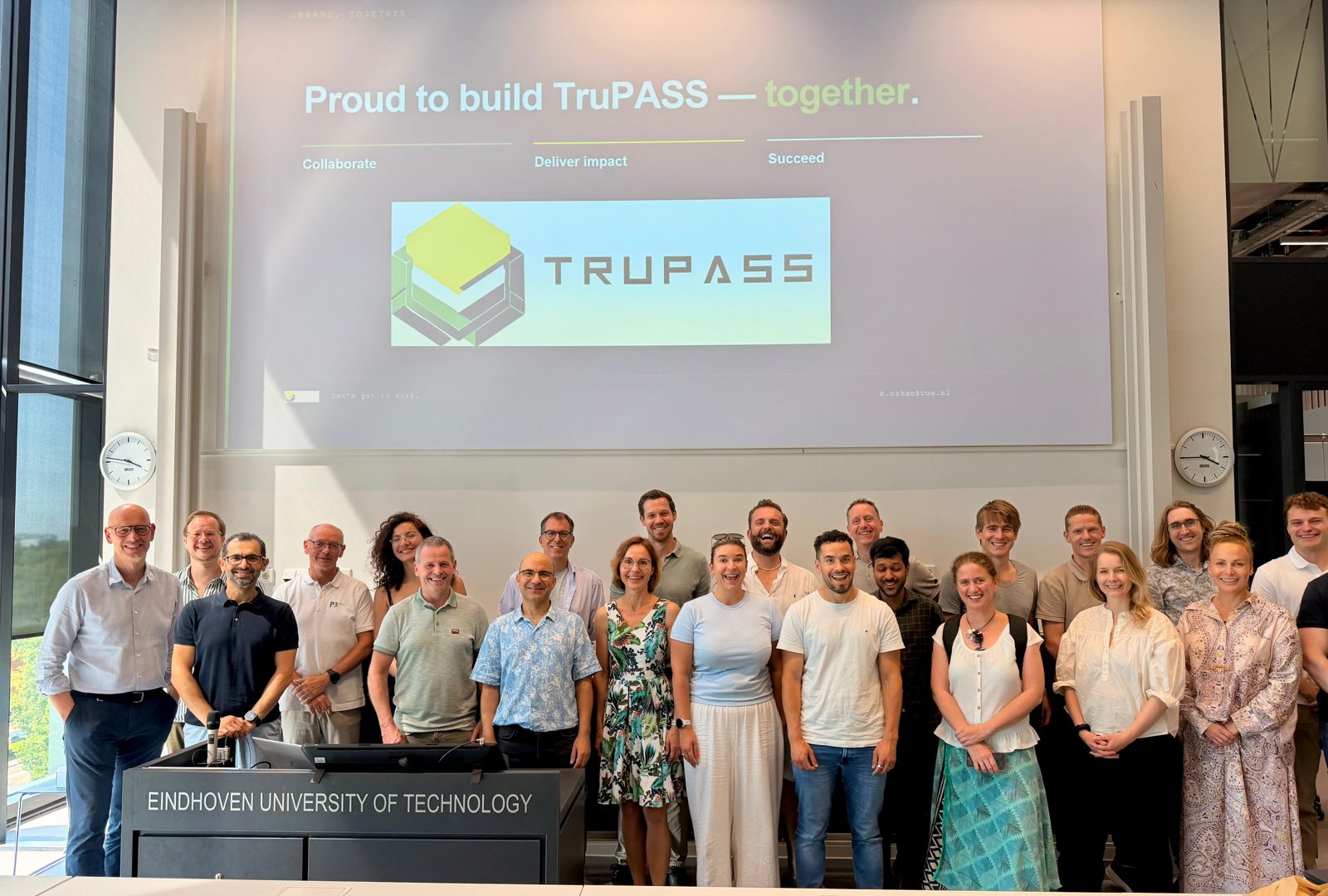 The TruPASS consortium standing together in a lecture hall at TU Eindhoven, with the TruPASS logo on the screen behind them